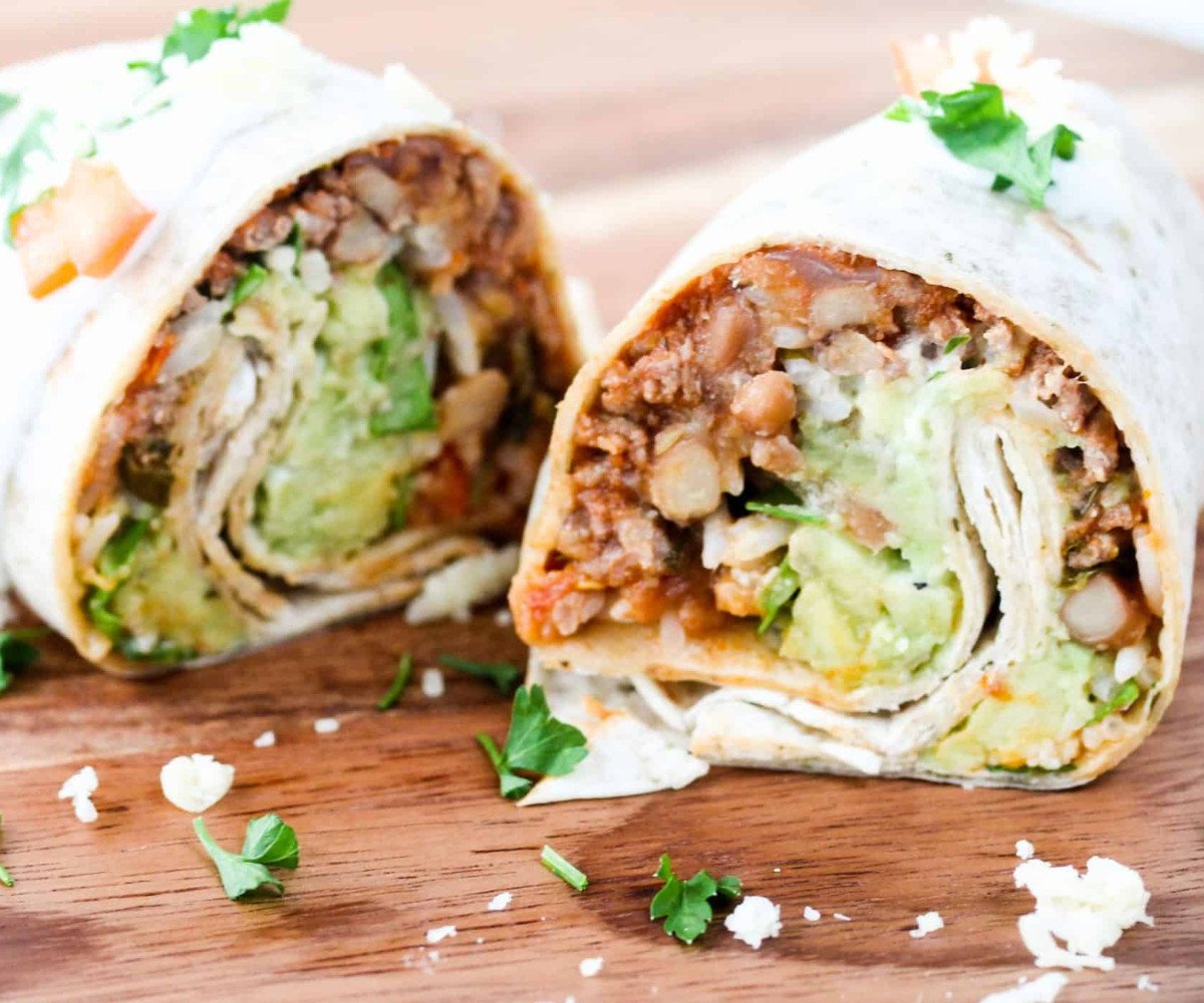 Beef burrito on a wooden choppin board with a wedge of lemon.