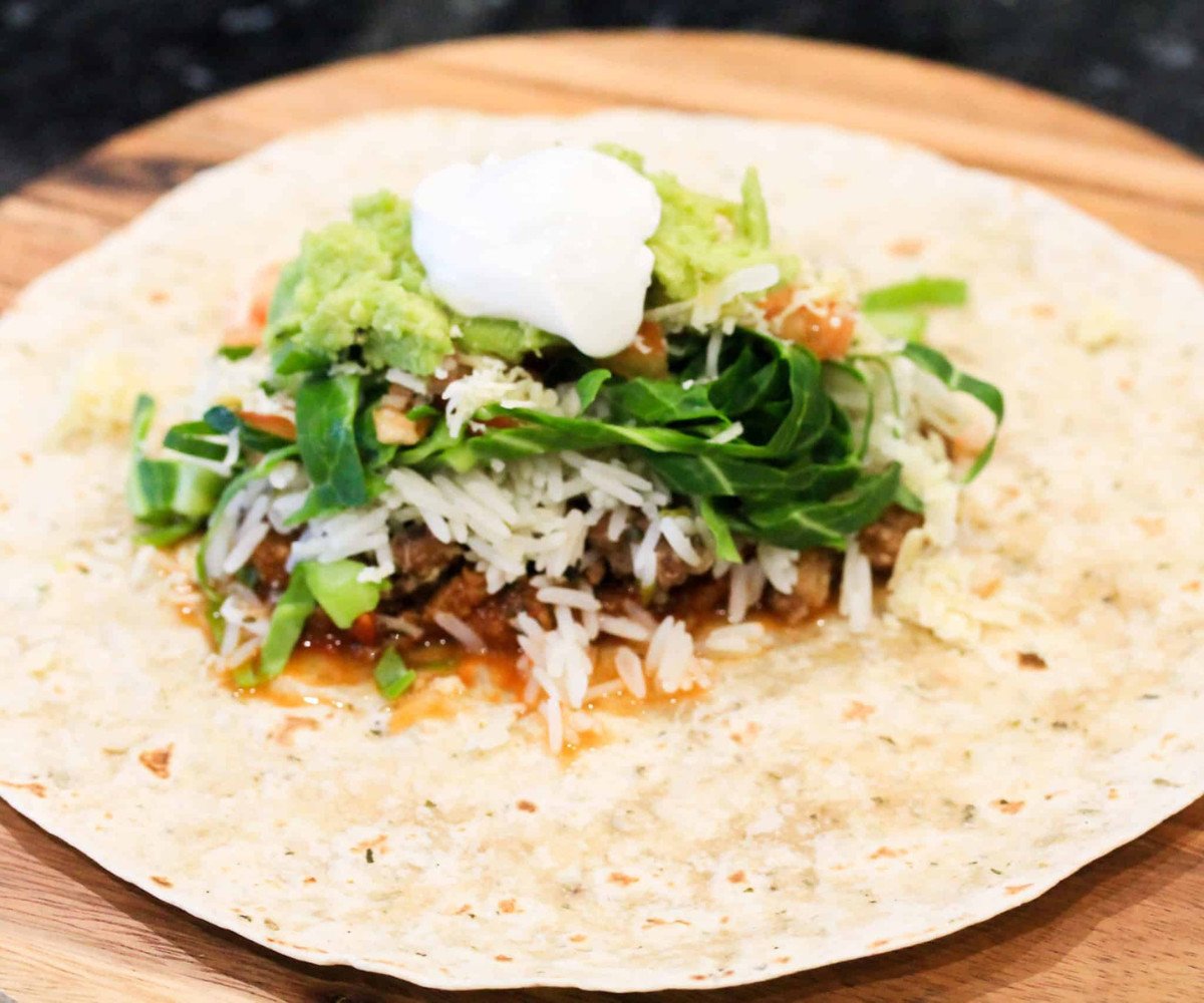 Burrito chopped in half on a chopping board with a wedge of lemon.