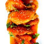 Hot wings on a white plate garnished with herbs and sesame seeds.