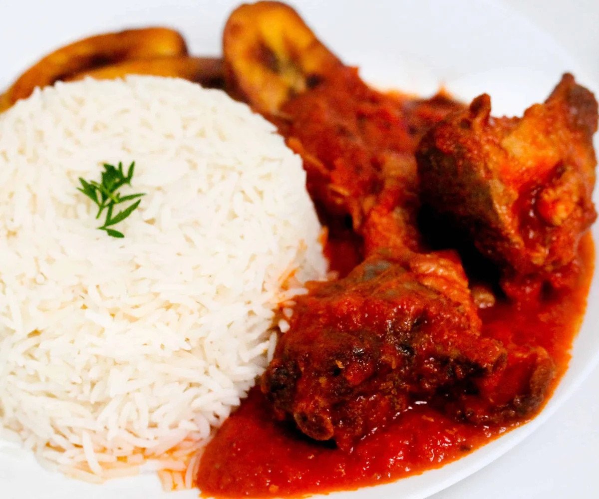 African red stew with chicken, beef, rice and plantain on a plate.