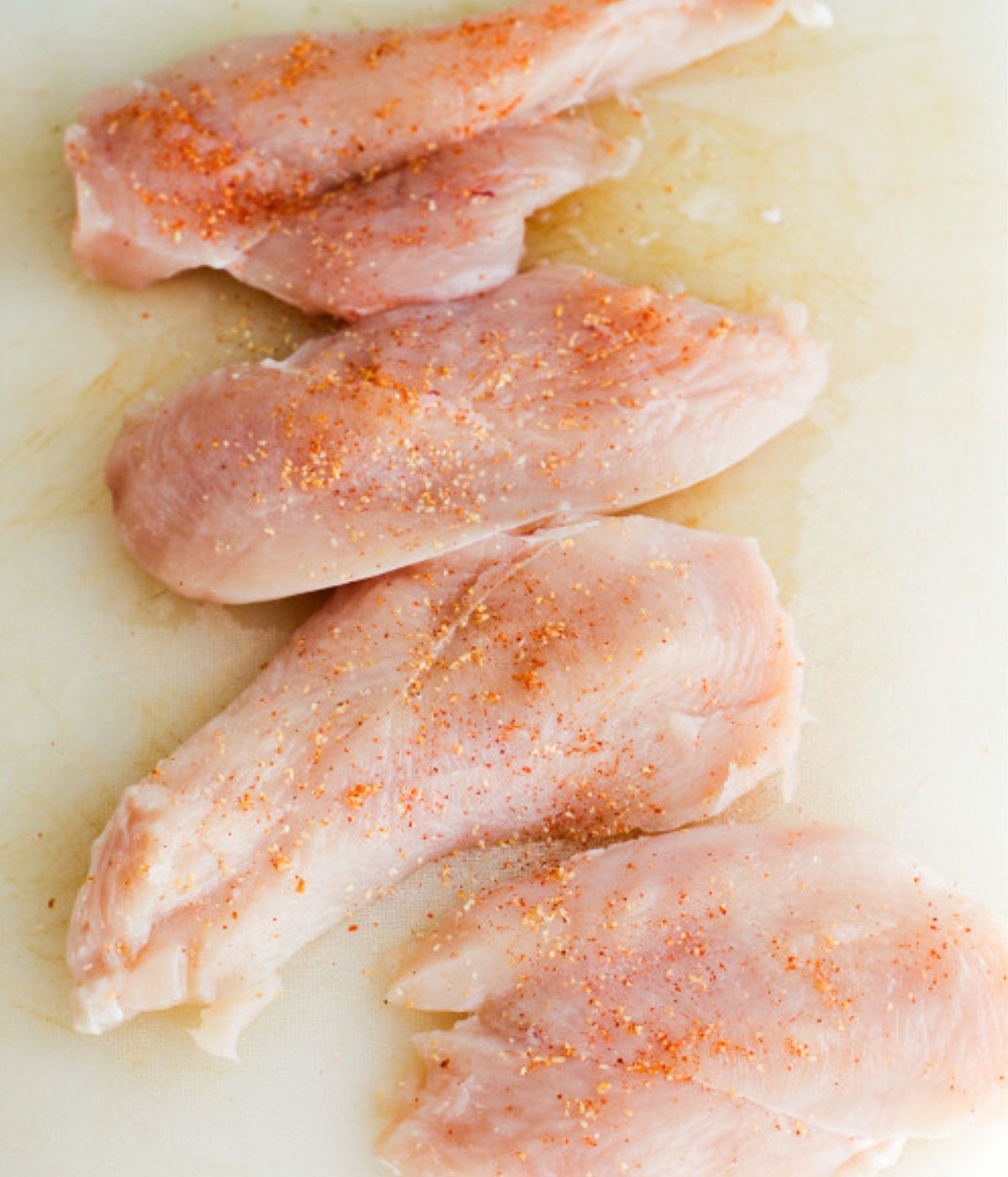 Chicken breasts on a white chopping board with seasoning.