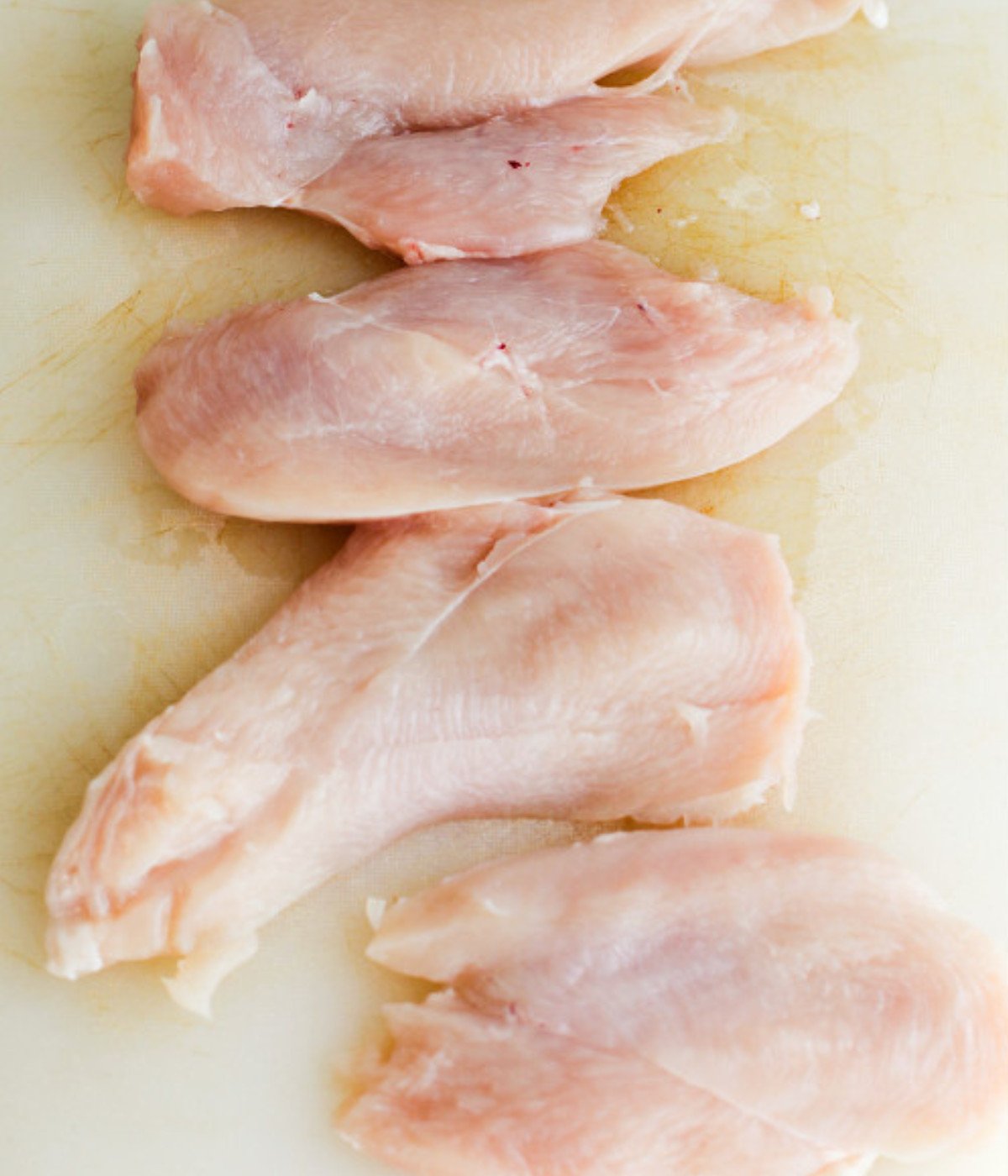 Chicken breasts on a white chopping board.