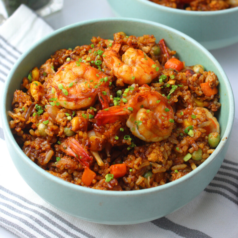 Chinese shrimp fried rice topped with scallions in a green bowl.