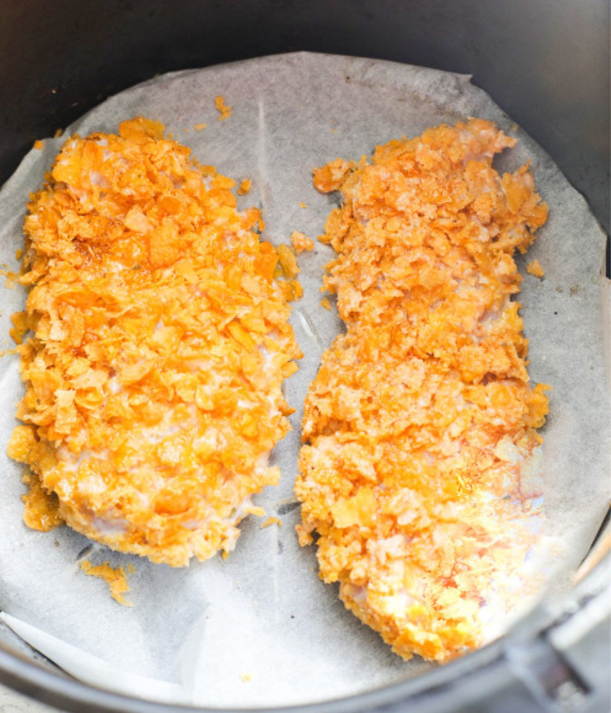 Cornflake coated chicken in a lined air fryer.