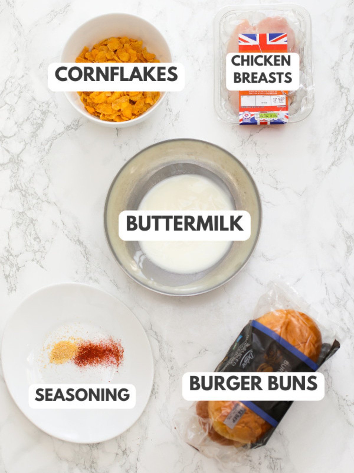 Cornflakes, chicken breasts, buttermilk, seasoning and burger buns on a table.