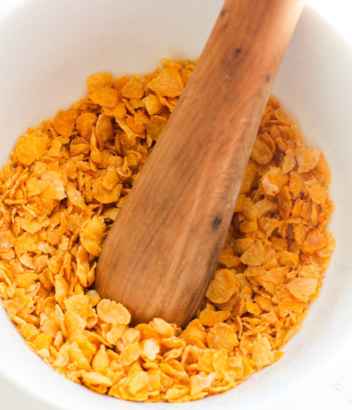 Cornflakes, salt and black pepper crushed with a wooden spoon in a white bowl.
