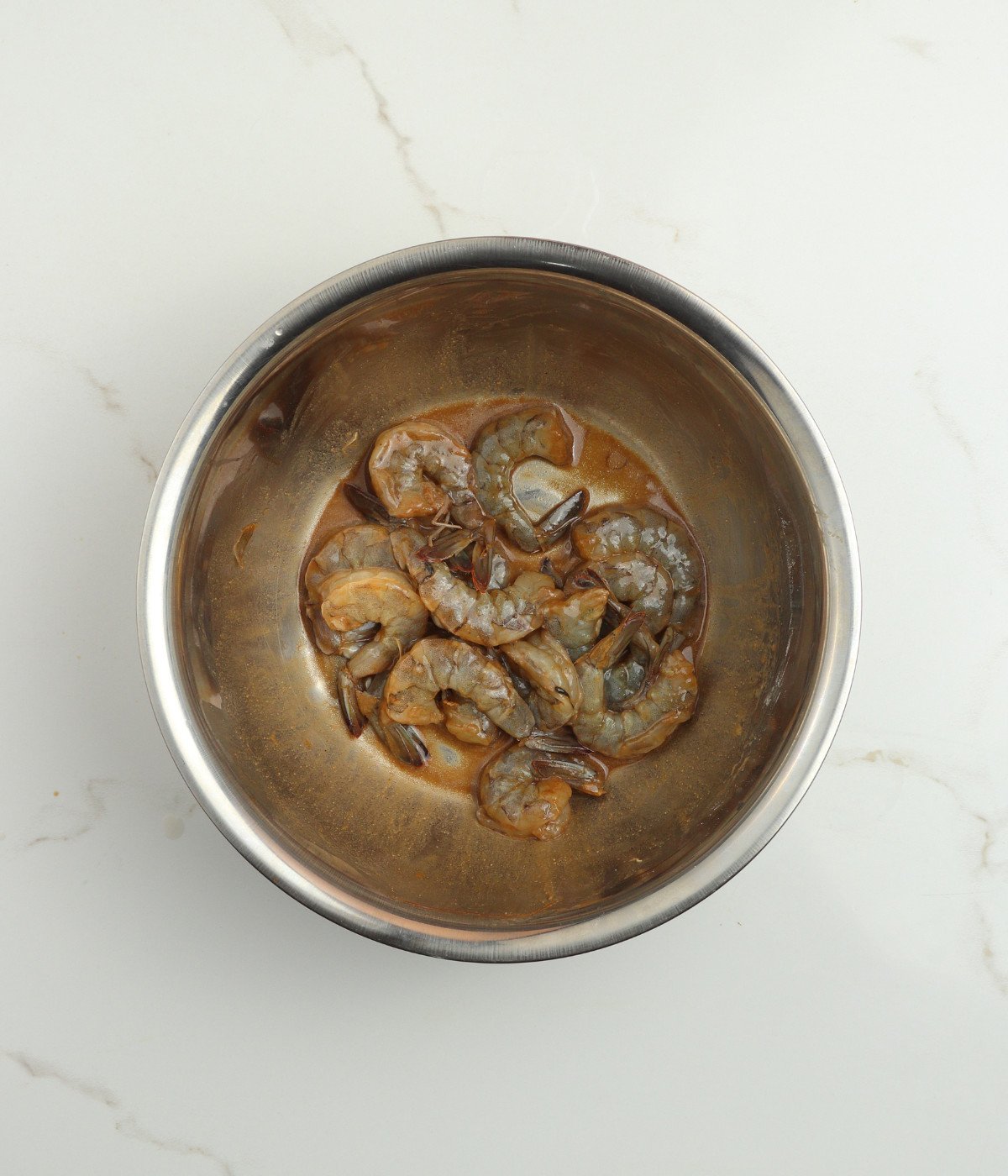 Marinated uncooked shrimp in a silver bowl.