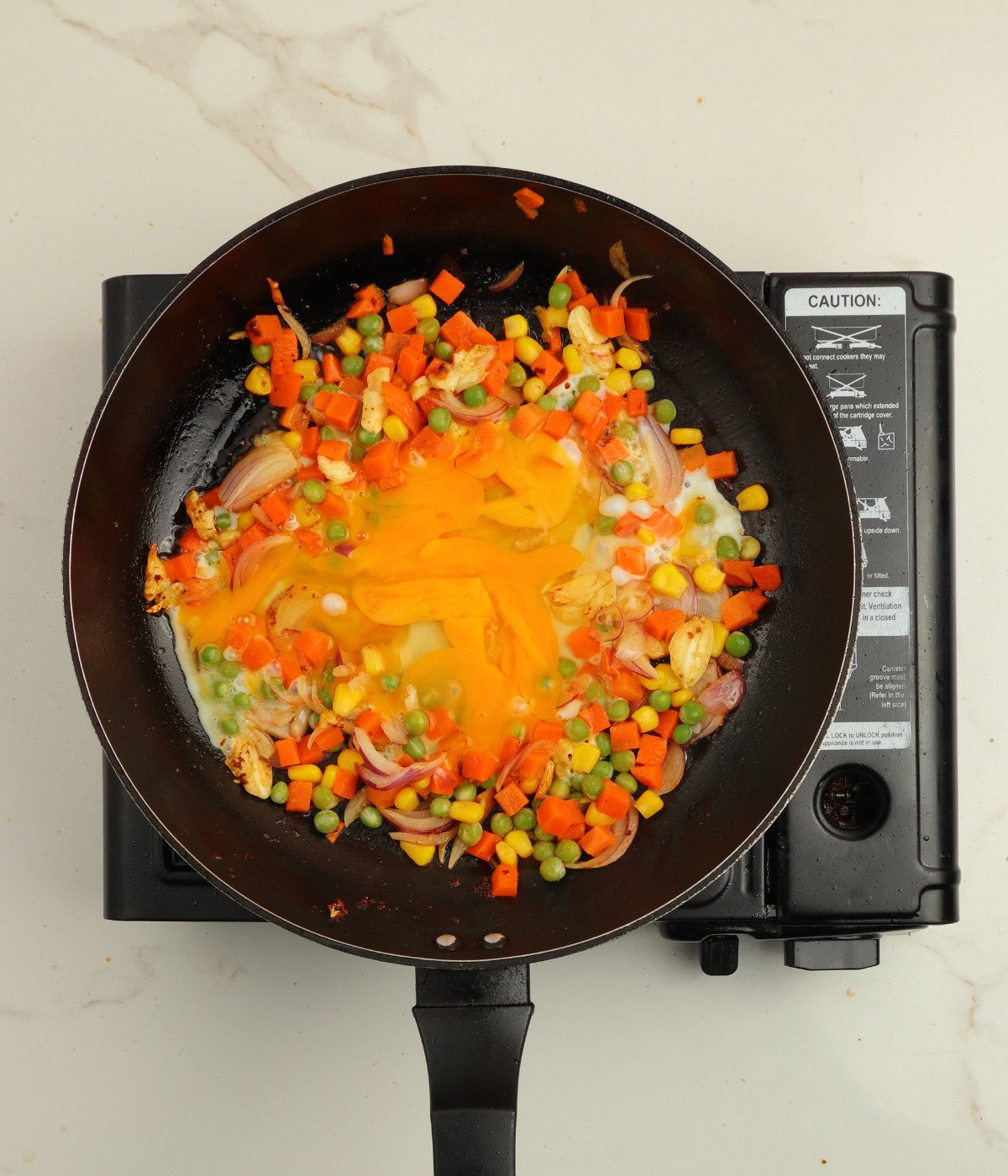 Mixed vegetables, onions and eggs cooked in a black pan.