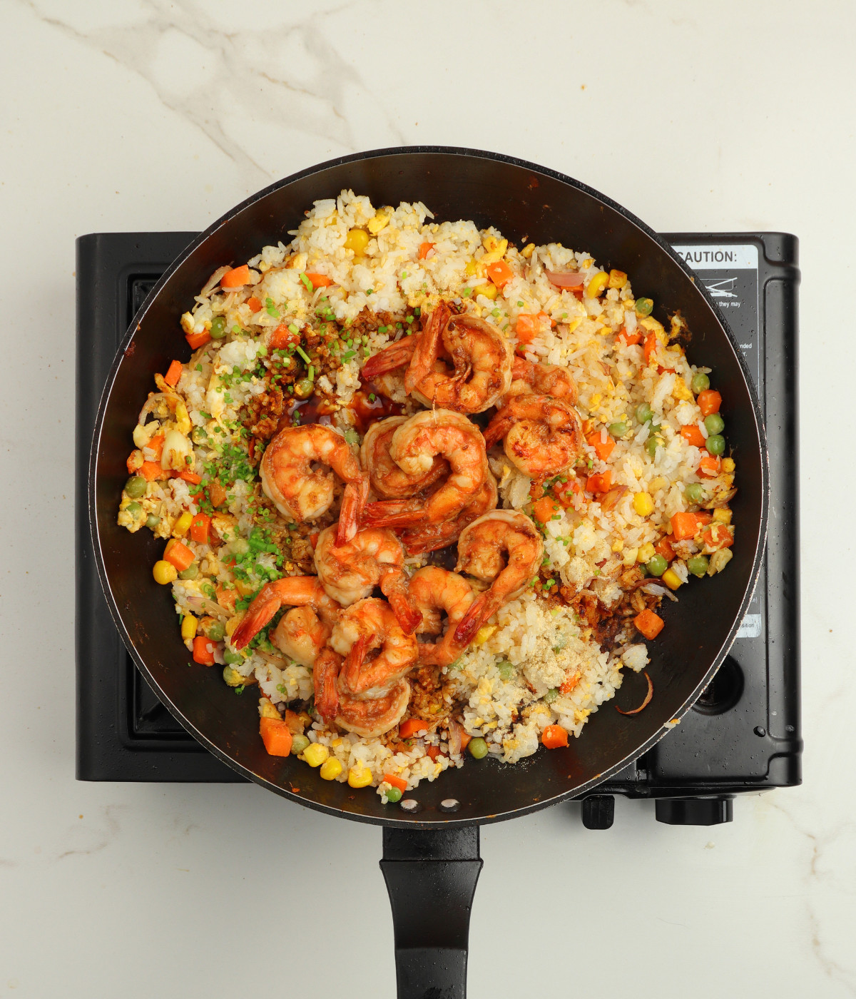 Mixed vegetables, onions, leftover white rice, soy marinade and eggs in a black pan.