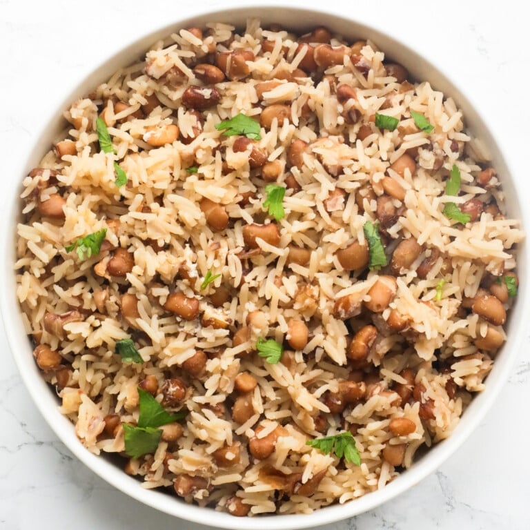 Nigerian rice and beans in a white plate topped with chopped parsley.