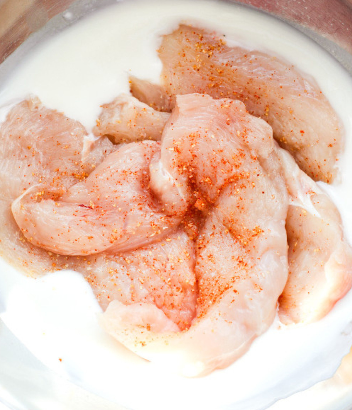 Seasoned chicken breasts and buttermilk in a silver bowl.
