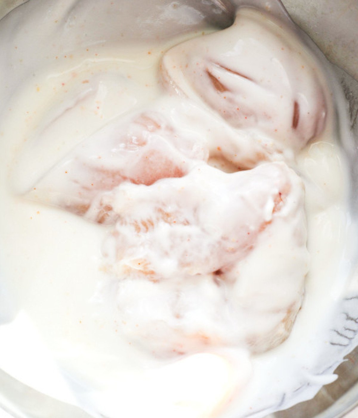 Seasoned chicken breasts and buttermilk mixed in a silver bowl.
