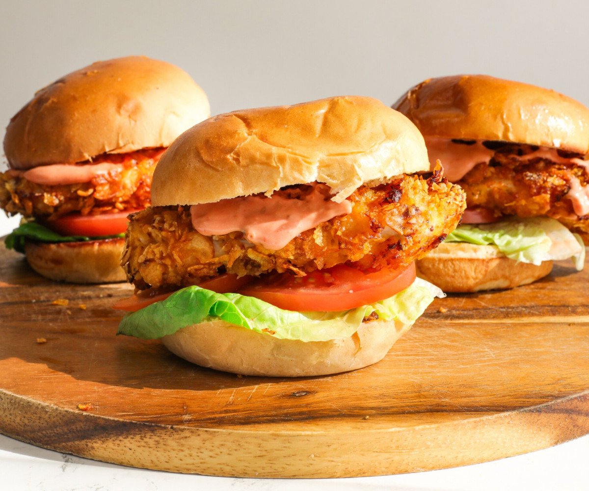 Three chicken burgers with lettuce and tomato on a wooden board.