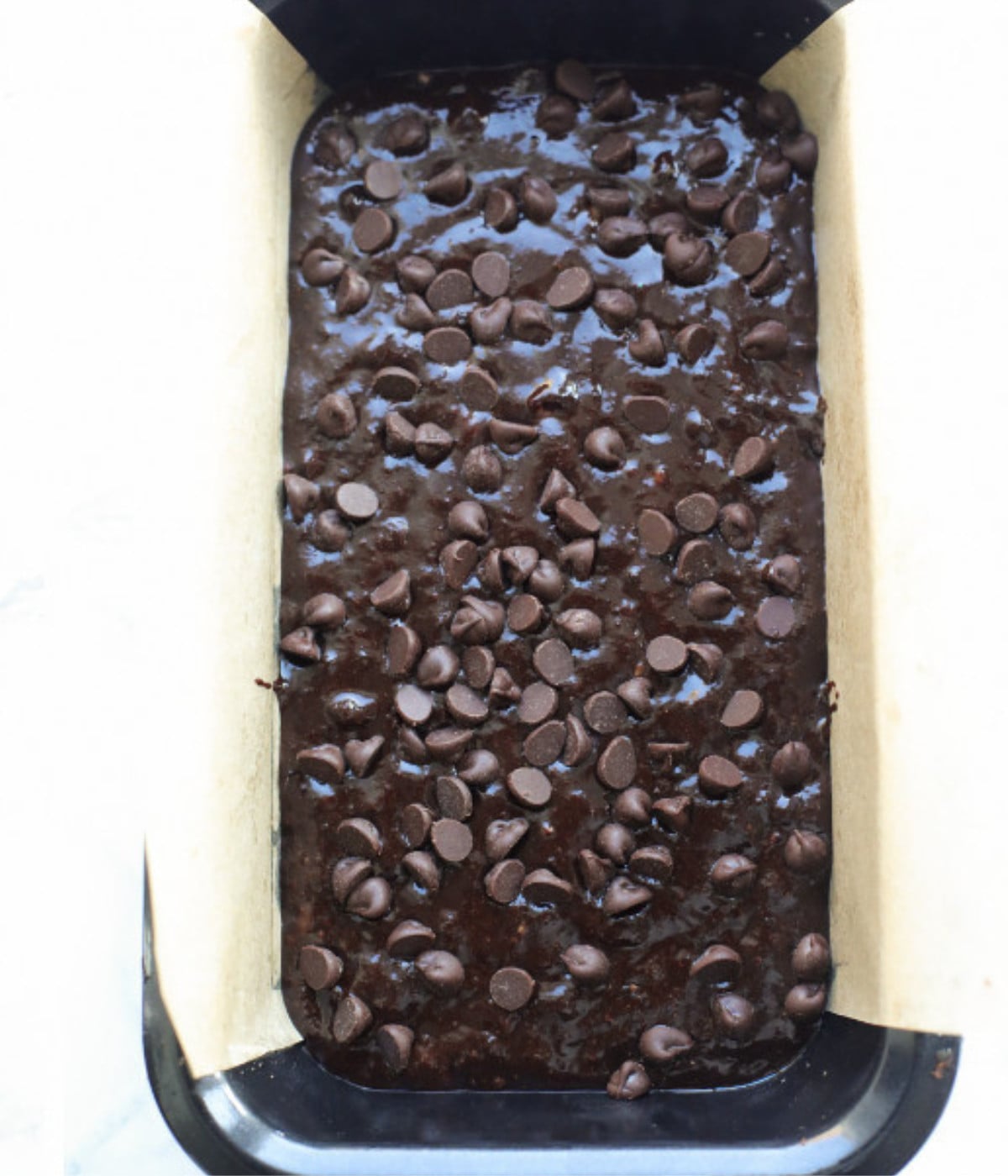 Chocolate banana bread batter with chocolate chips on top in a lined loaf tin.
