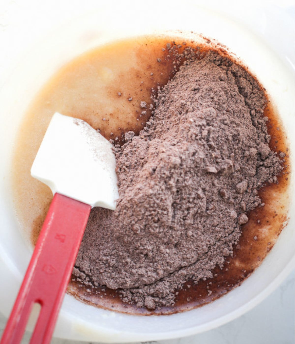 Egg, mashed banana, cocoa powder, flour in a bowl with a spatula.