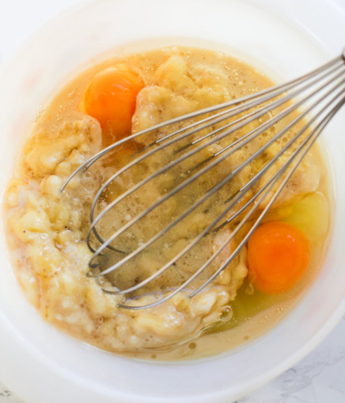 Oil, eggs and mashed bananas mixed in a bowl.