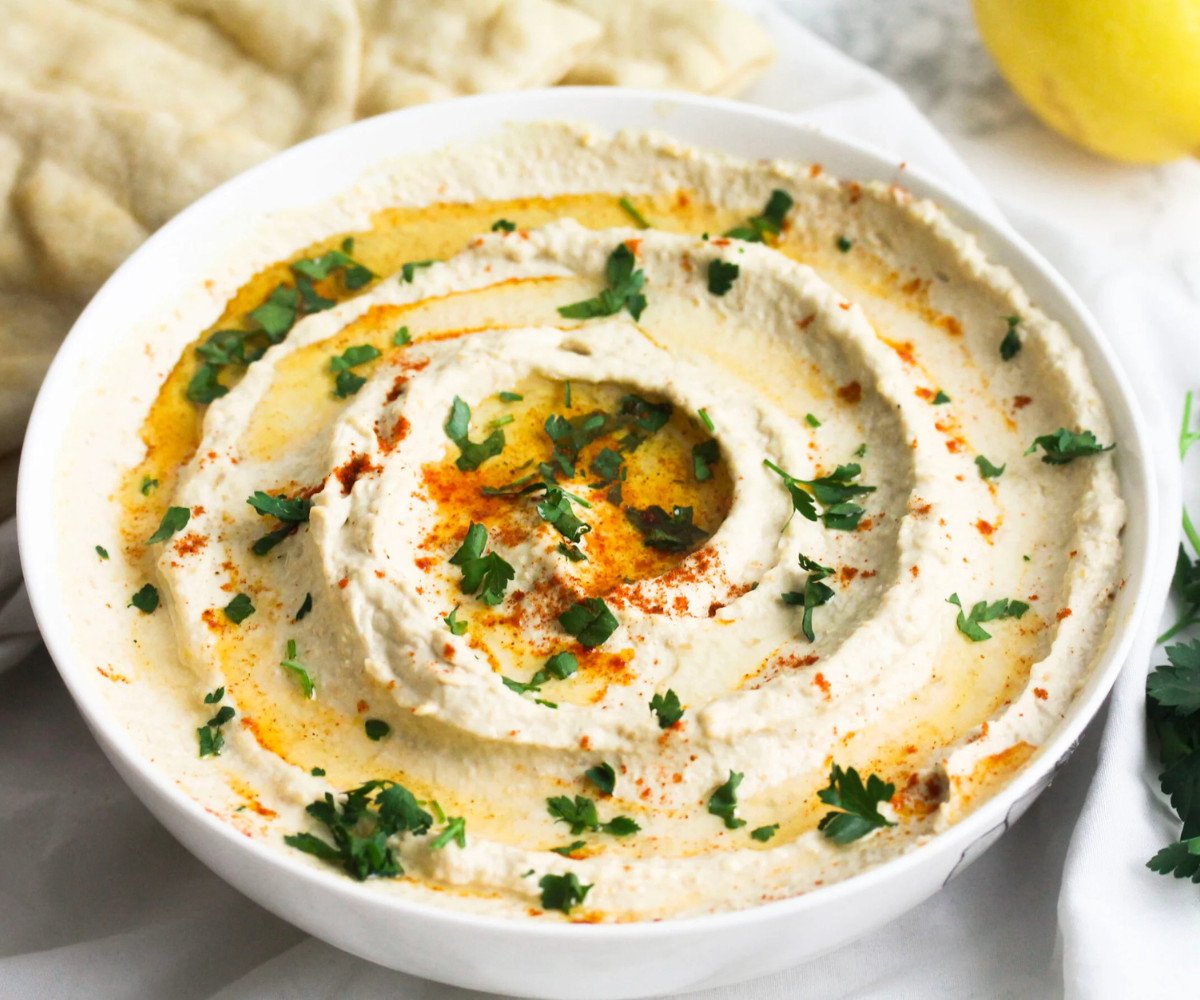 Hummus in a white bowl with oil, paprika and parsley on top.