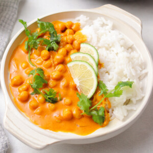 Chickpea curry, white rice, lime and parsley in a white bowl.