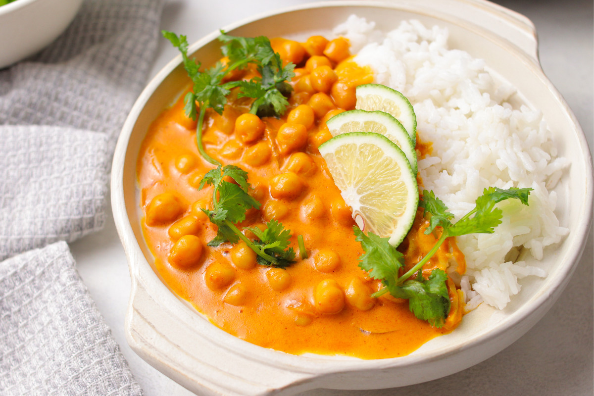 Chickpea curry, white rice, lime wedges and fresh herbs in a white bowl.