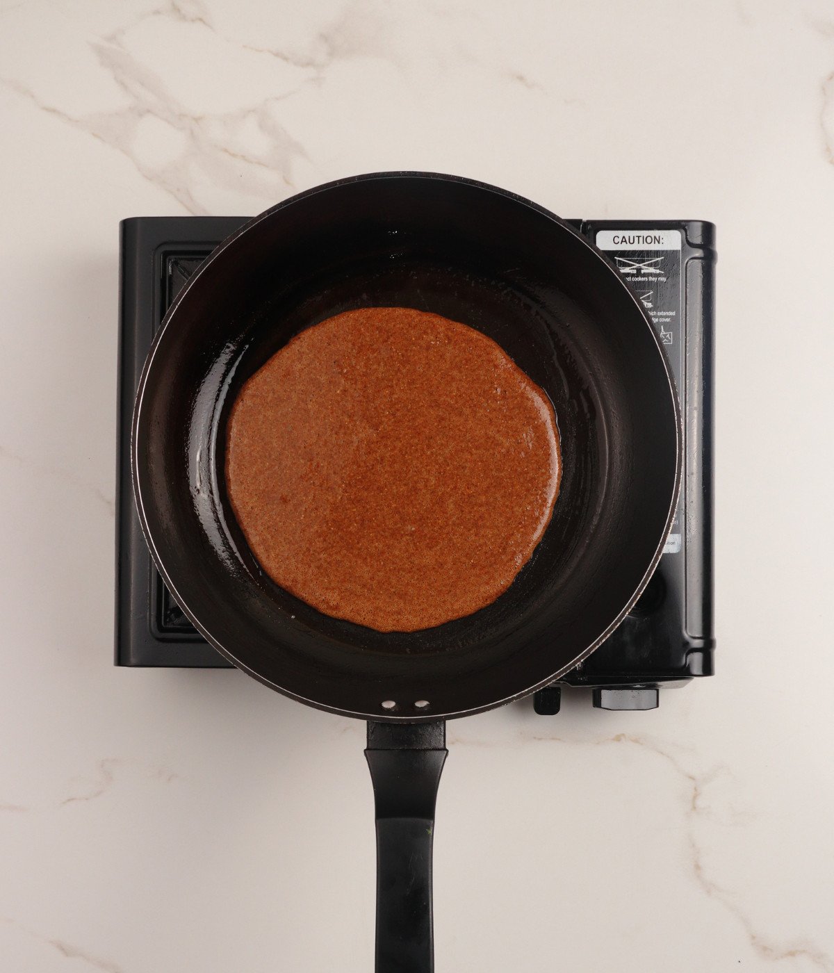 Chocolate pancake batter cooking in a pan.