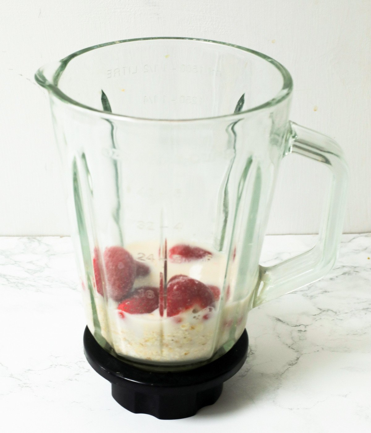 Frozen strawberries, oats and milk in a smoothie maker.