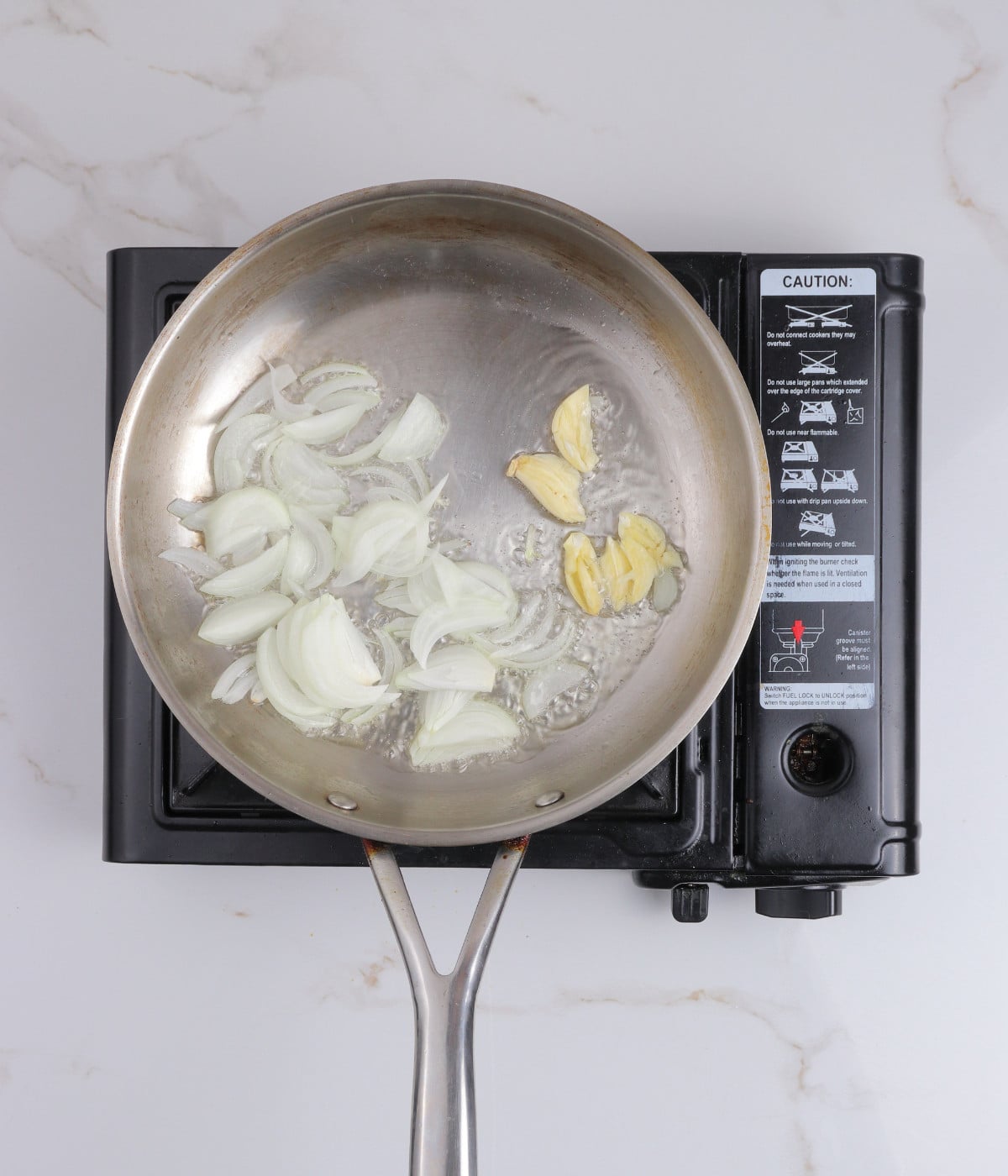 Onions and garlic cooking in oil in a silver pan.