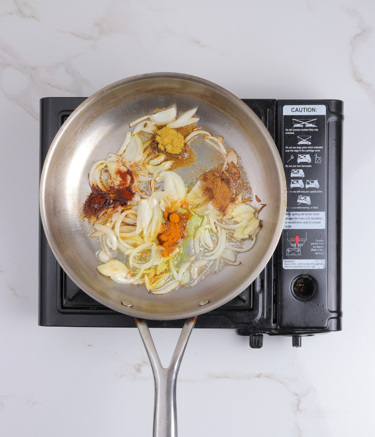 Onions, garlic, cumin, curry, corriander, paprika cooking in oil in a silver pan.