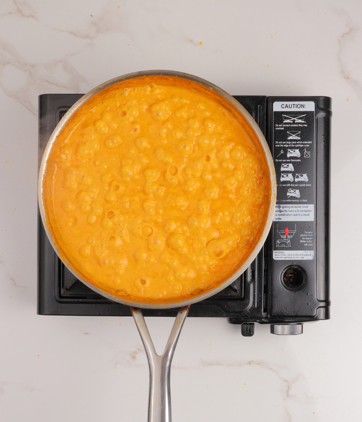 Seasoning, coconut milk and chickpeas mixed and cooking in a silver pan.