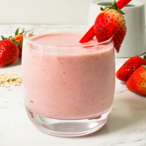 Strawberry oat smoothie in a glass cup with a red straw and strawberry.