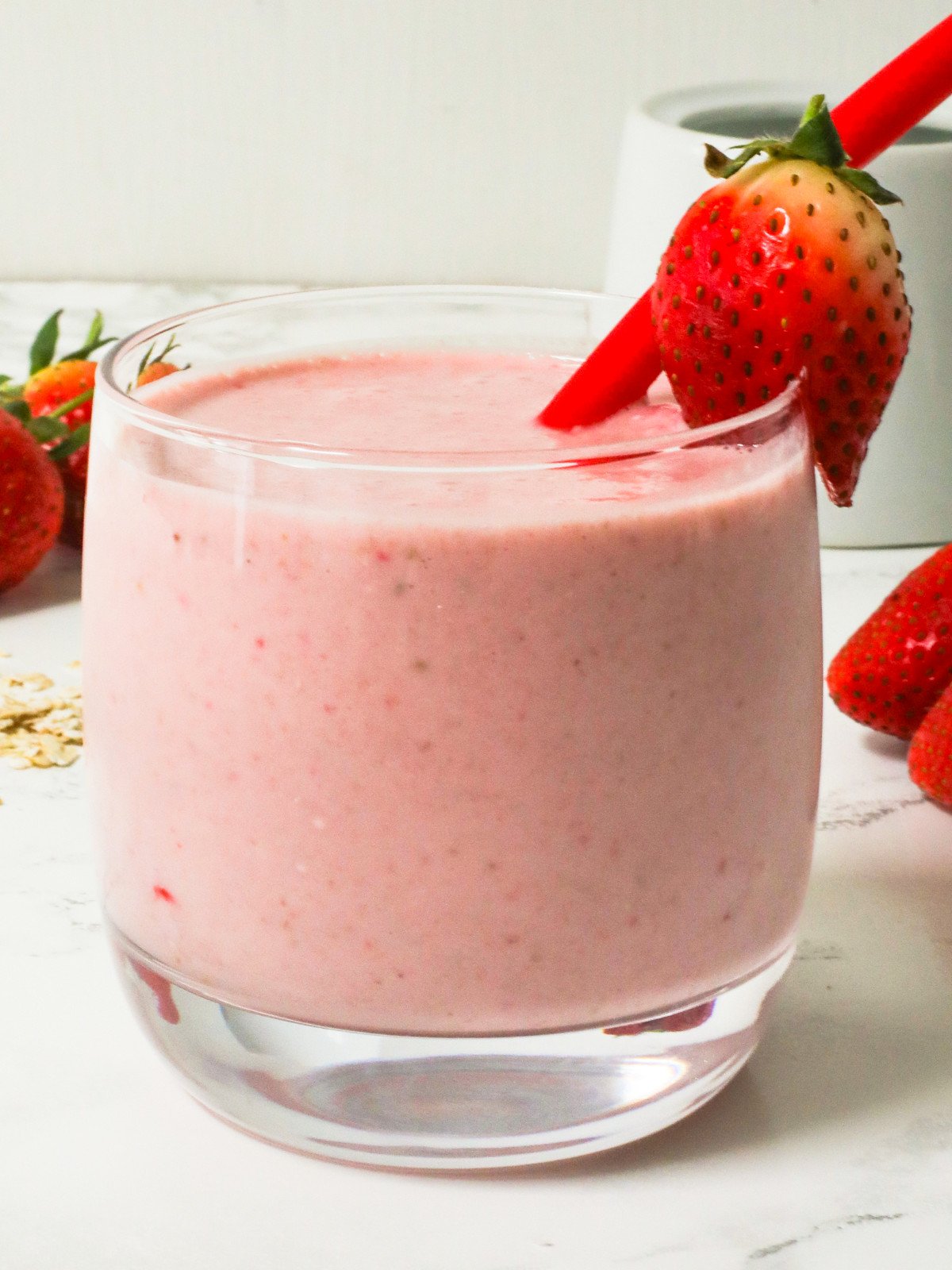 Strawberry oats smoothie in a glass cup with a strawberry and red straw.