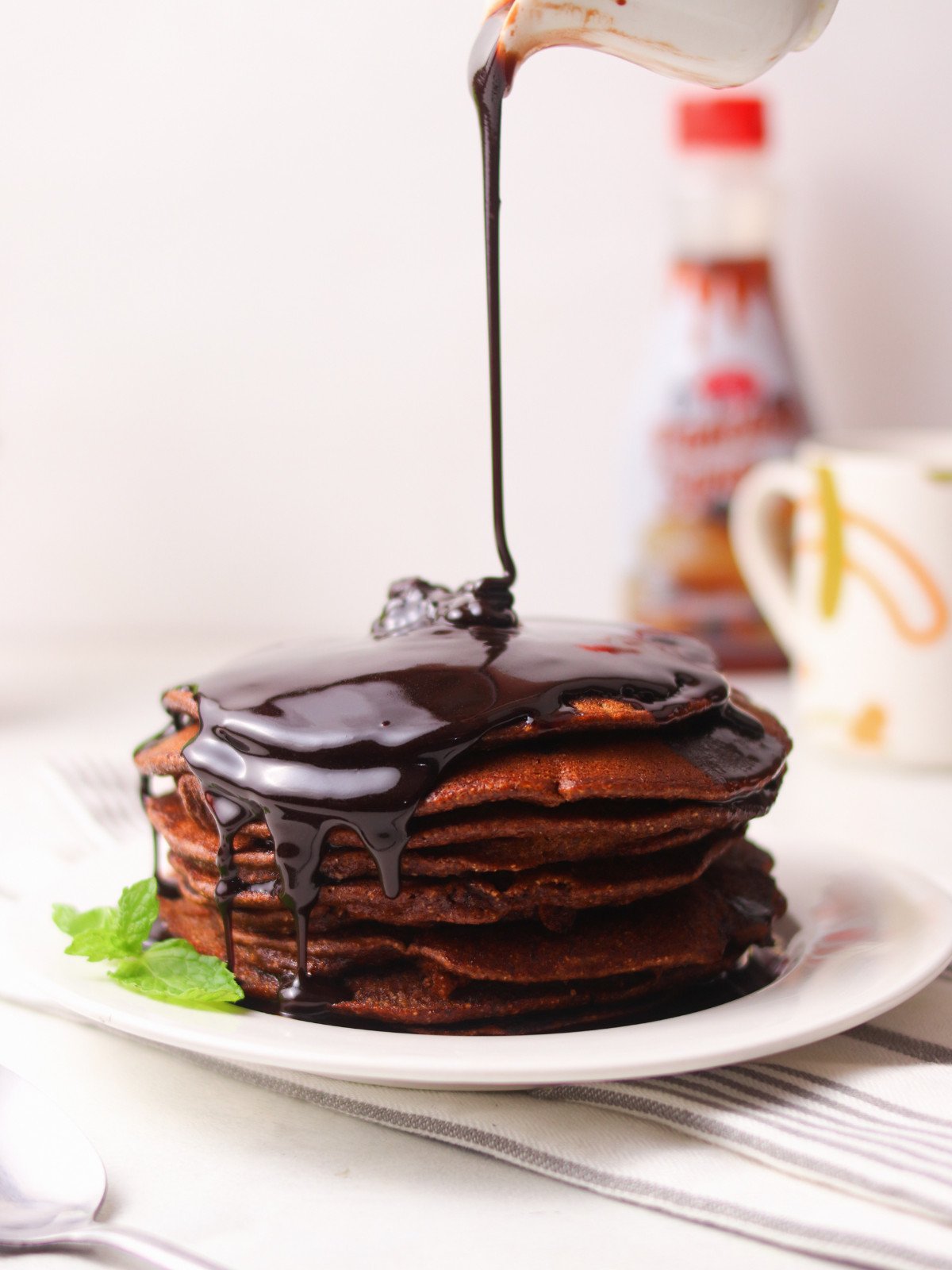 Wholewheat chocolate pancakes in a white plate with chocolate sauce poured on top.