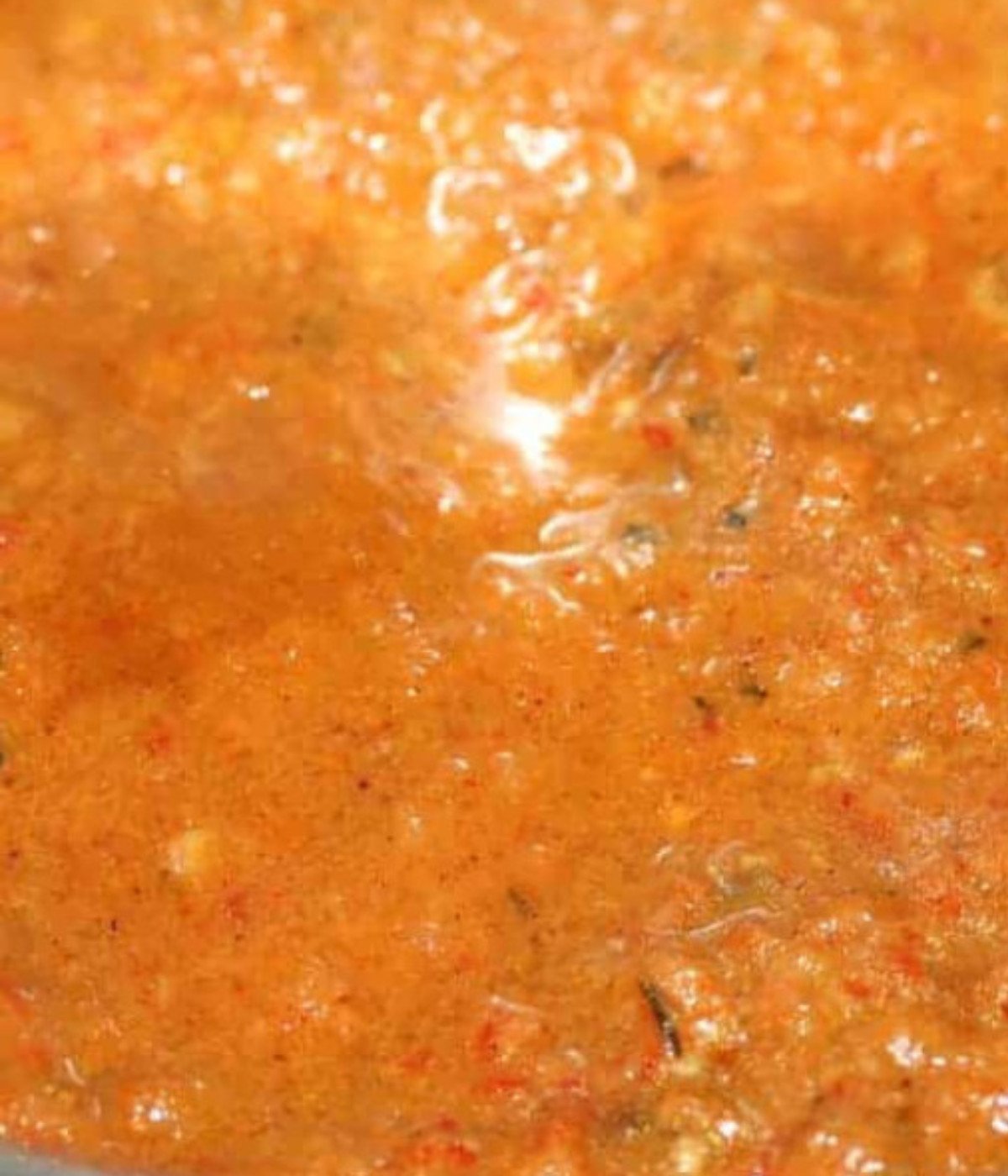Blended tomatoes and seasoning cooking in a silver pot.