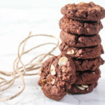Eight chocolate cookies with almond flakes on a white table and a rope.