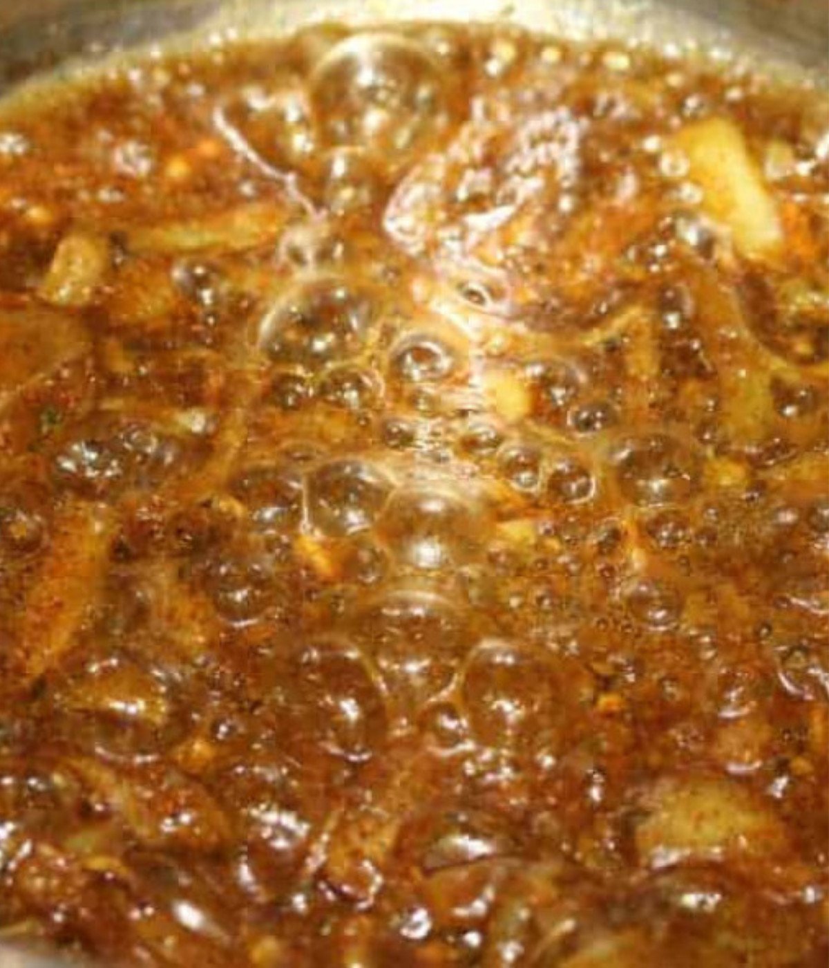 Mixed onions, herbs, and seasoning frying in a silver pot.