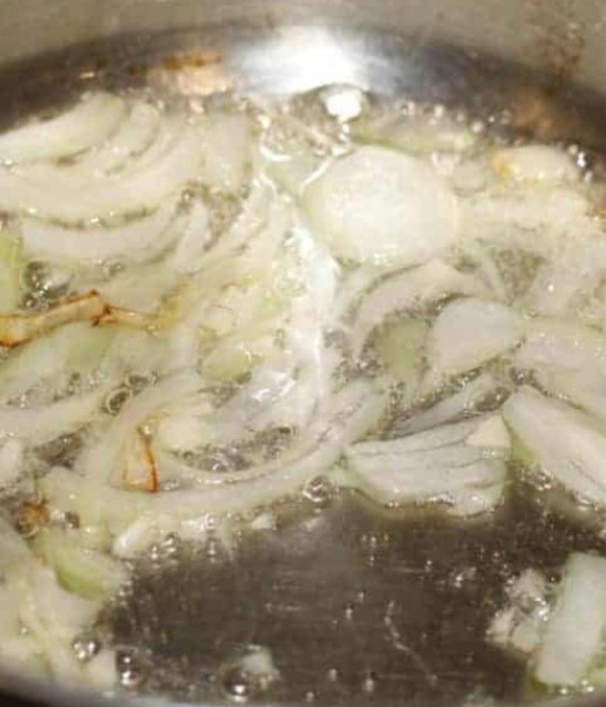 Onions frying in a silver pot.