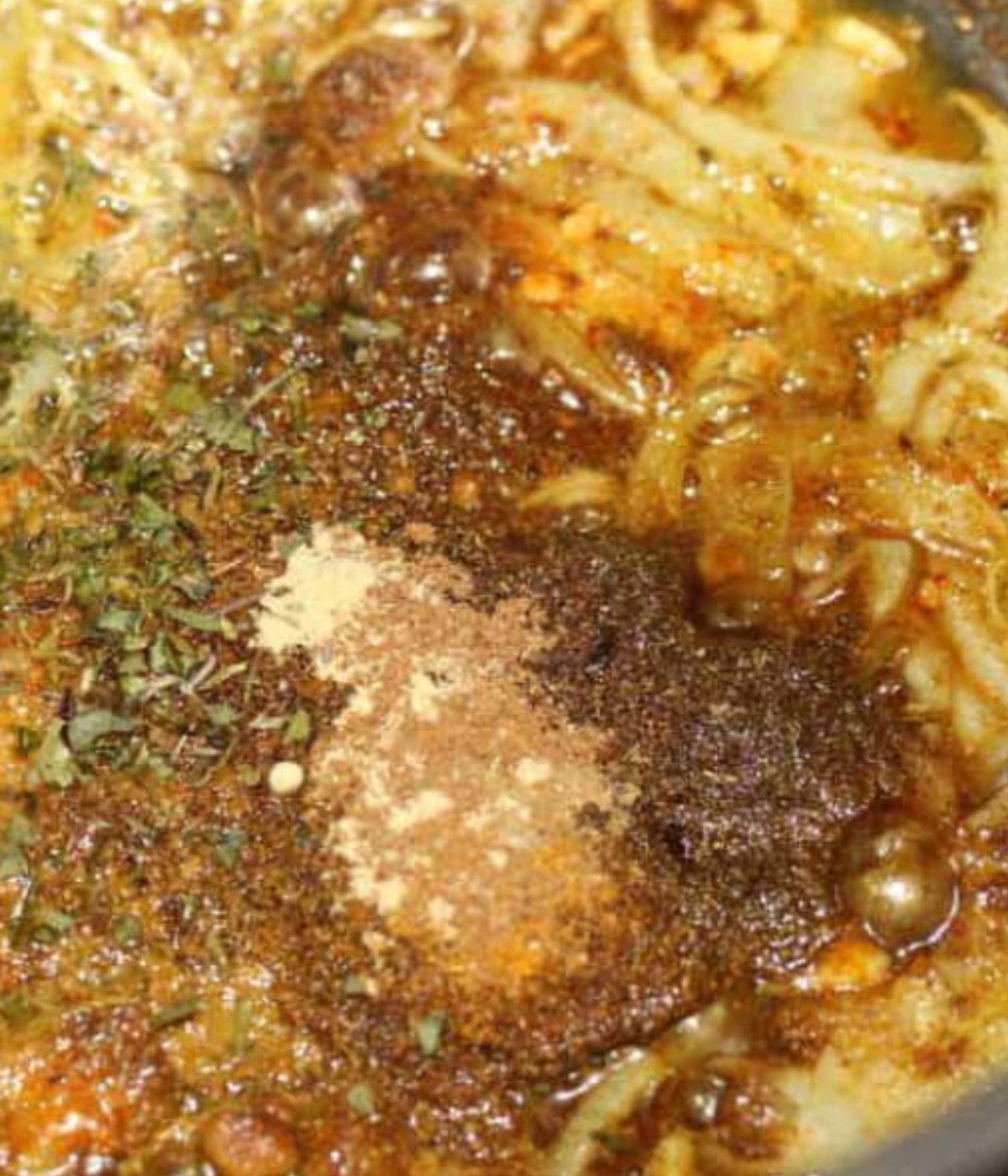 Onions, herbs, and seasoning frying in a silver pot.
