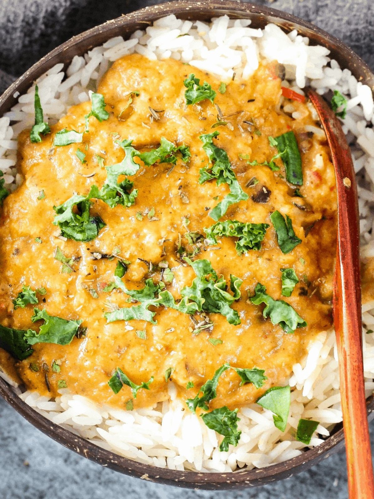 Red lentil curry and white rice topped with herbs in a bamboo bowl.