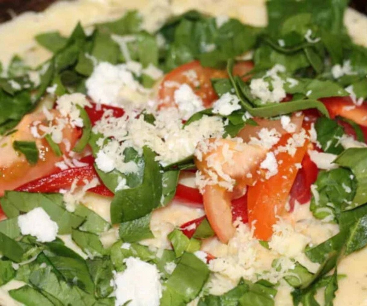 Vegetable omelette cooking on a pan topped with cheese.