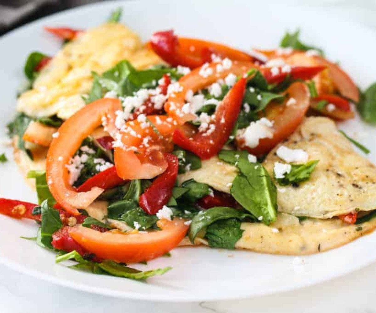 Vegetarian omelette topped with tomatoes, red capsicum peppers and spinach on a plate.