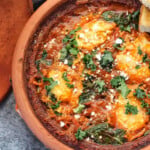 shakshuka in a brown pot garnished with feta and fresh herbs.