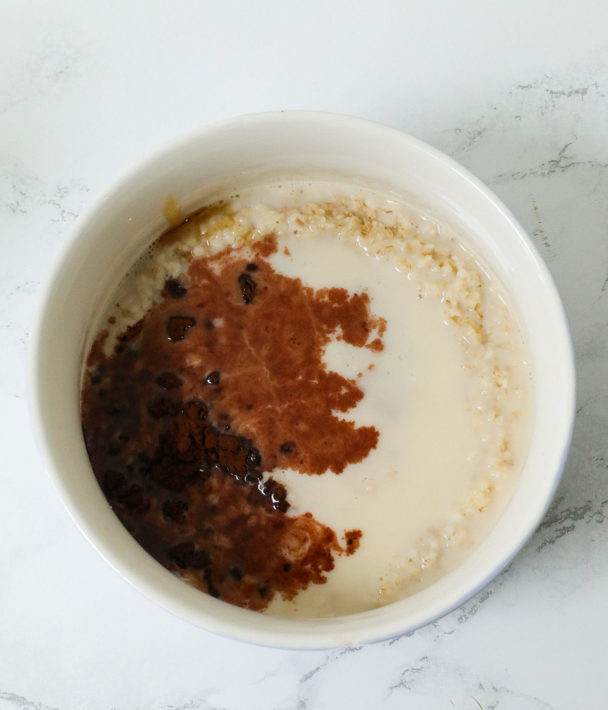 Cooked oats, cocoa powder and milk in a white bowl.