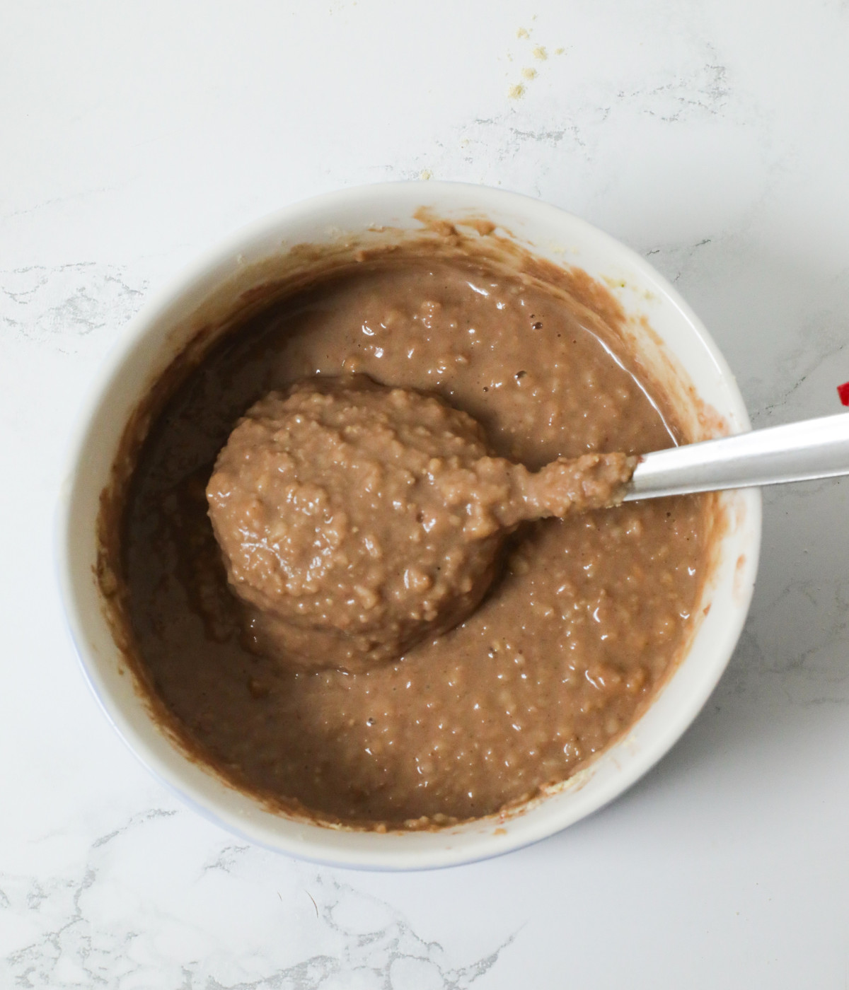 Cooked oats, cocoa powder and milk mixed completely in a white bowl with a spoon.