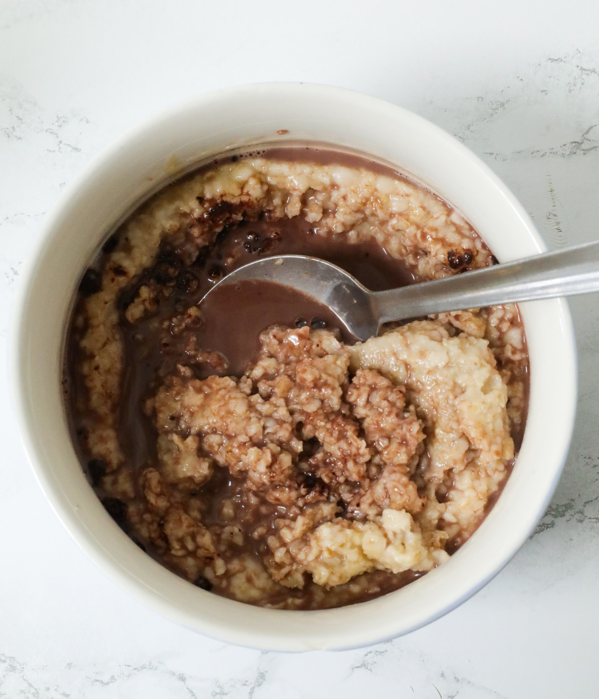 Cooked oats, cocoa powder and milk mixed in a white bowl with a spoon.