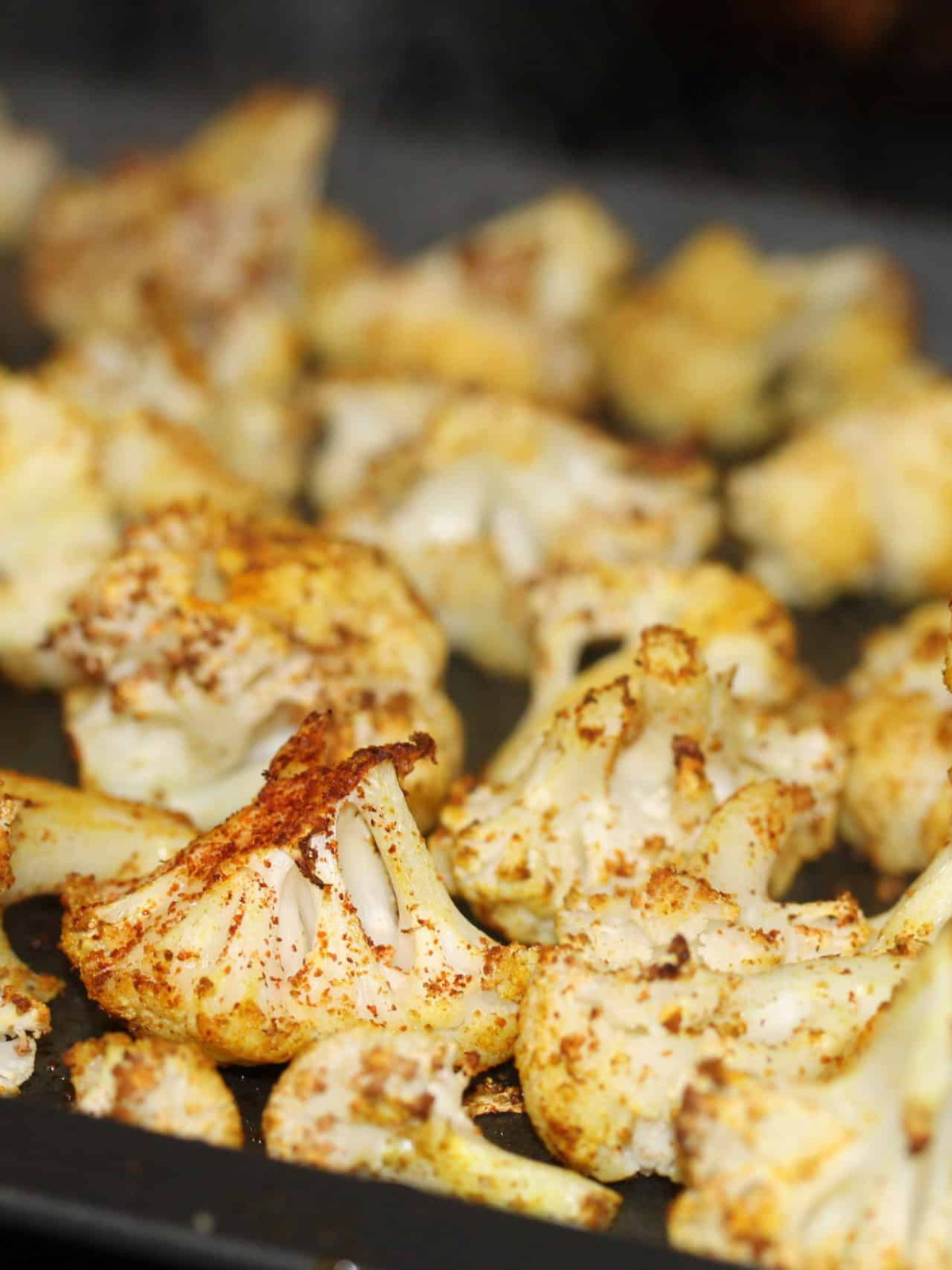 Spicy cumin and curry cauliflower florets on a baking tray.