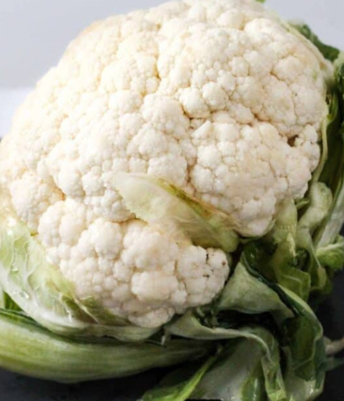 Whole white cauliflower with green stem on a chopping board.