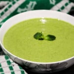 Broccoli soup in a white bowl with mint leaf on top.