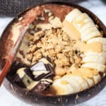 Chocolate oats, banana, granola and tahini in a bamboo bowl.