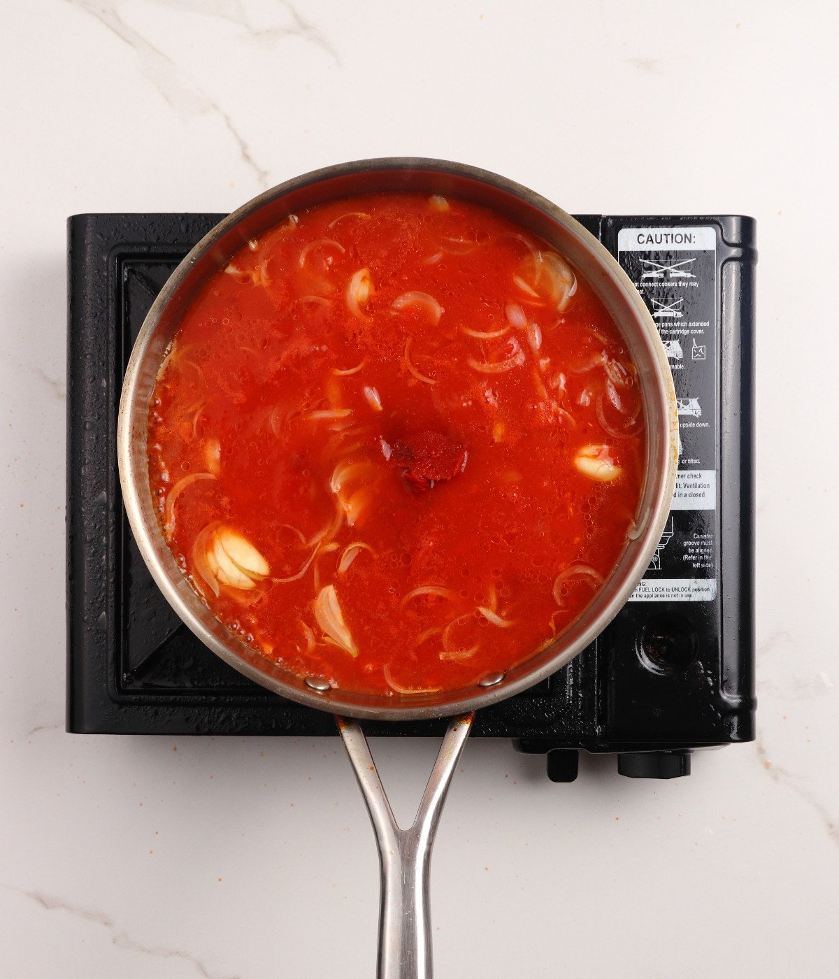 Chopped tomatoes, onion and tomato paste cooking in a silver pan.