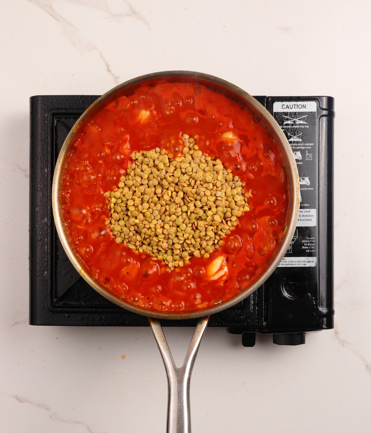 Chopped tomatoes, onion, seasoning and green lentils cooking in a silver pan.
