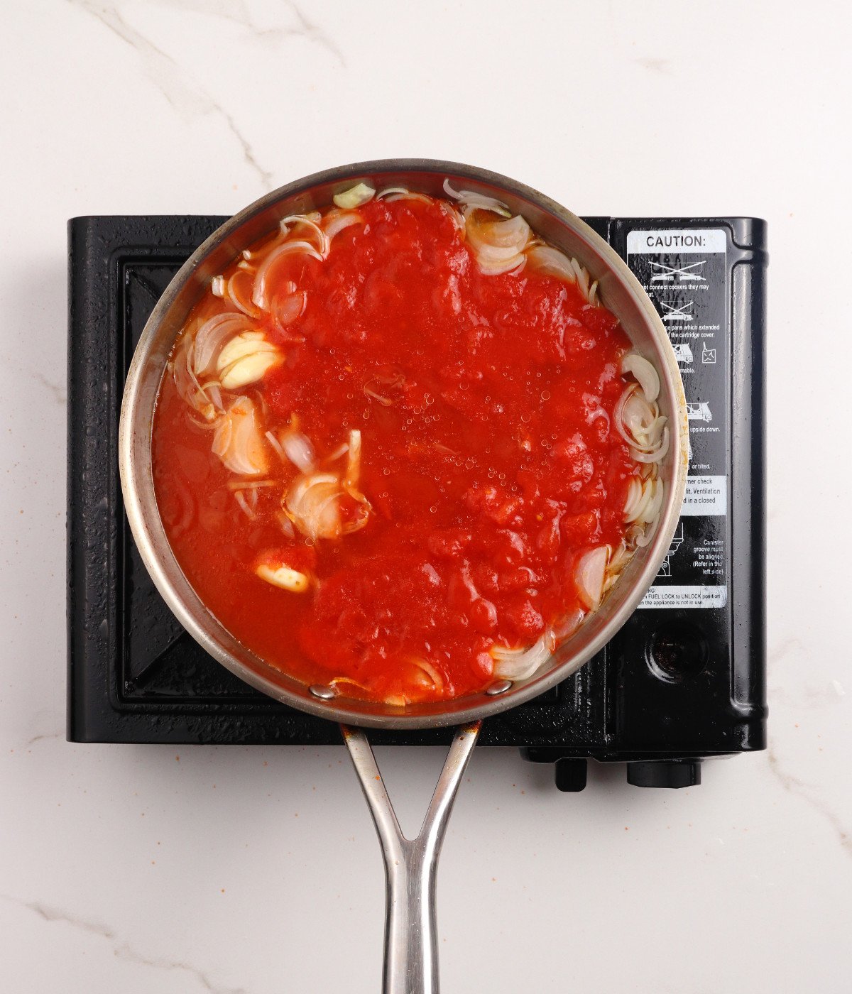 Chopped tomatoes, onion, seasoning and mixed cooking in a silver pan.